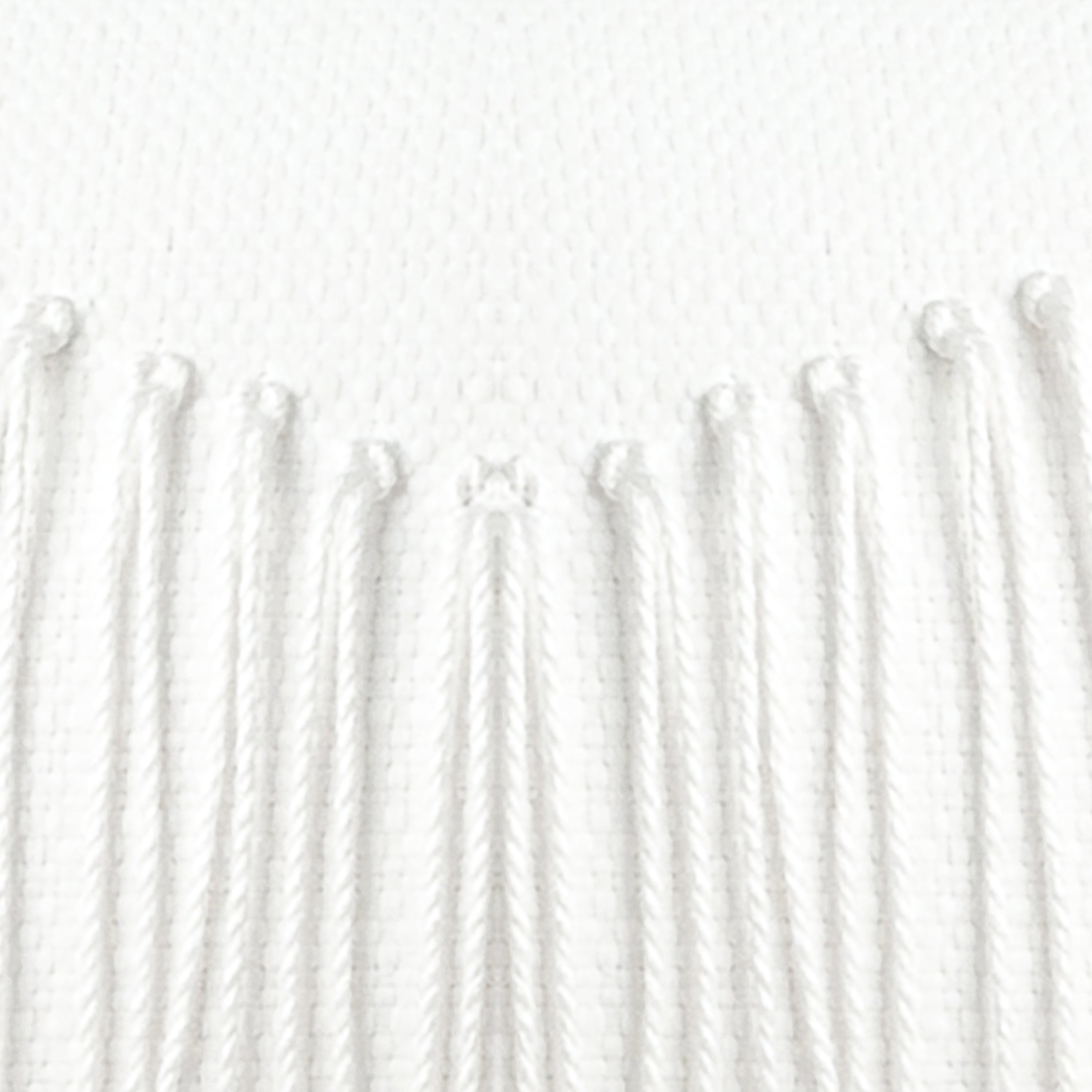 Detail image of White textured outdoor pillow with fringe details and tassels on top corners for modern indoor and outdoor decor by Elaine Smith