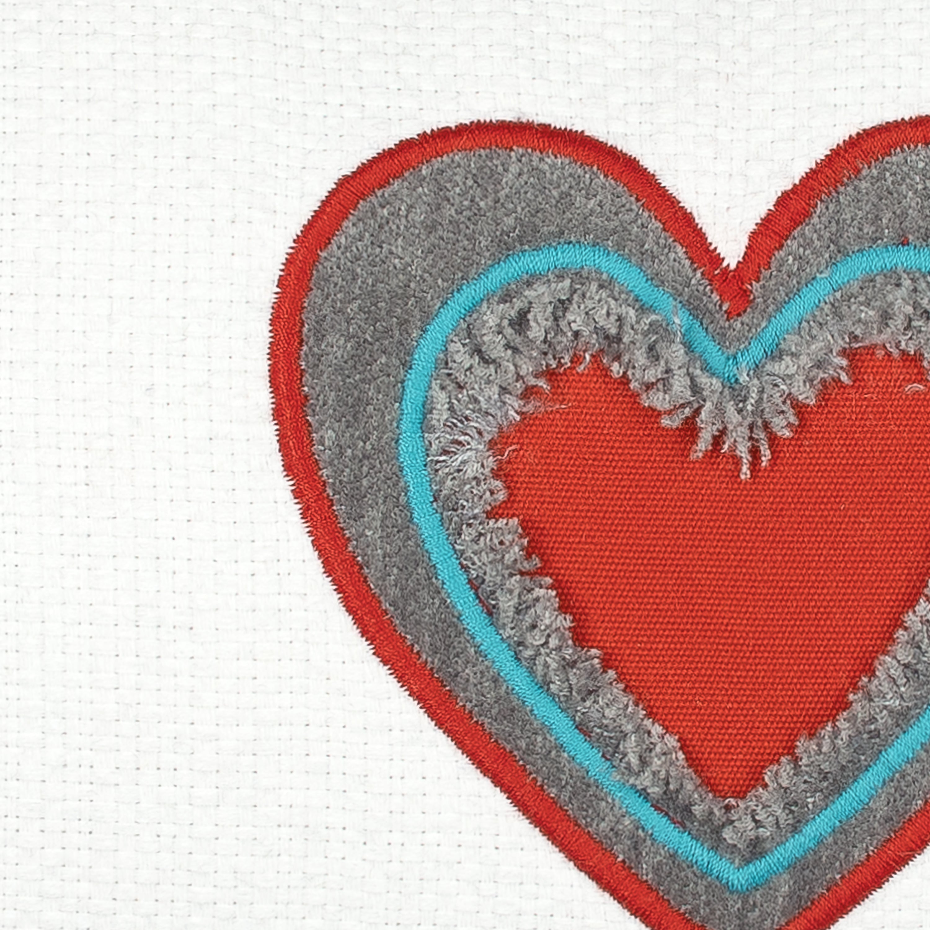 Detail image of White pillow with cut out heart in red and gray and aruba tassels in western theme.
