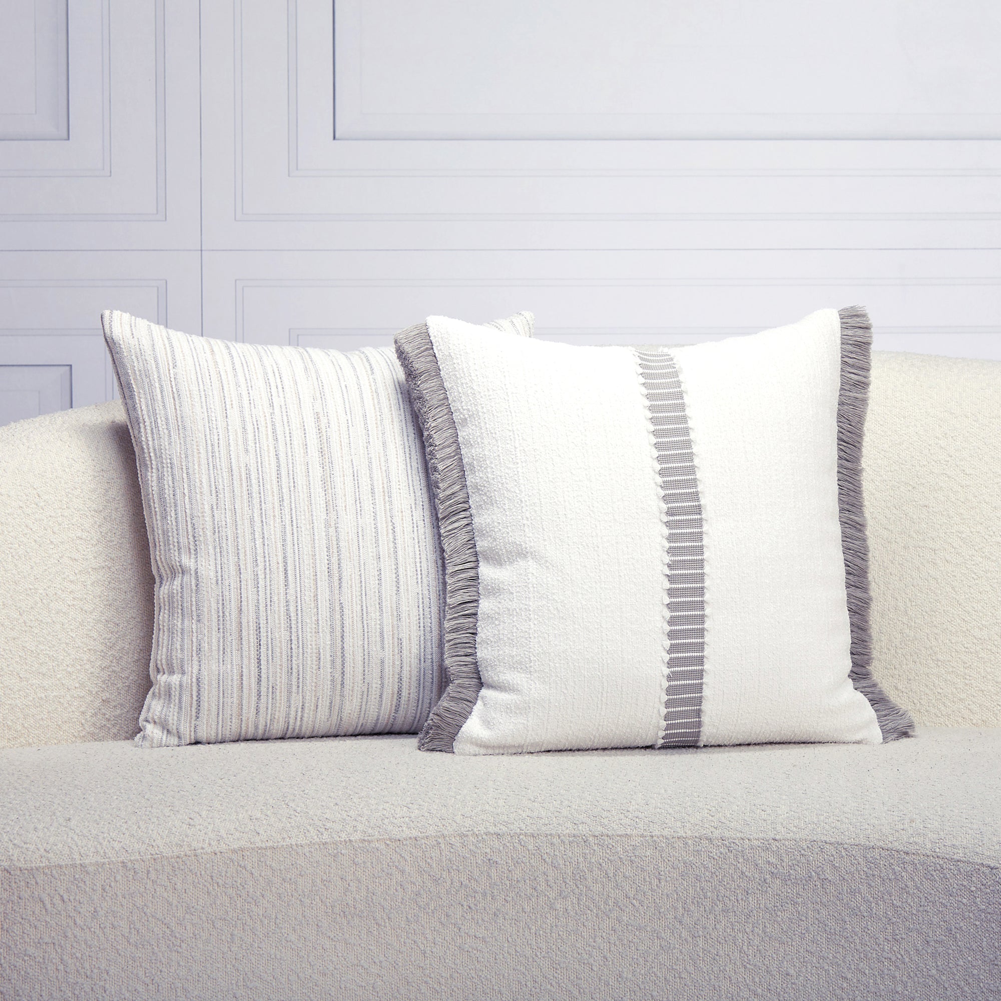 Two decorative pillows with striped patterns on a light gray sofa against a light gray wall.