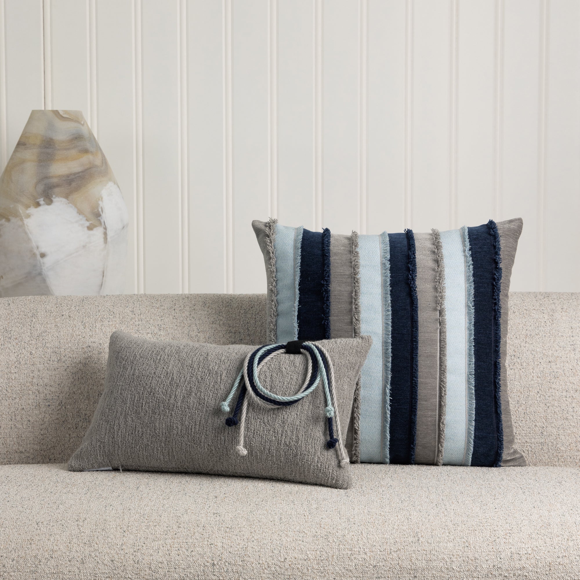 Pieced striped accent pillow by elaine smith in navy, gray and light blue and gray lumbar with rope detailing on ivory sofa