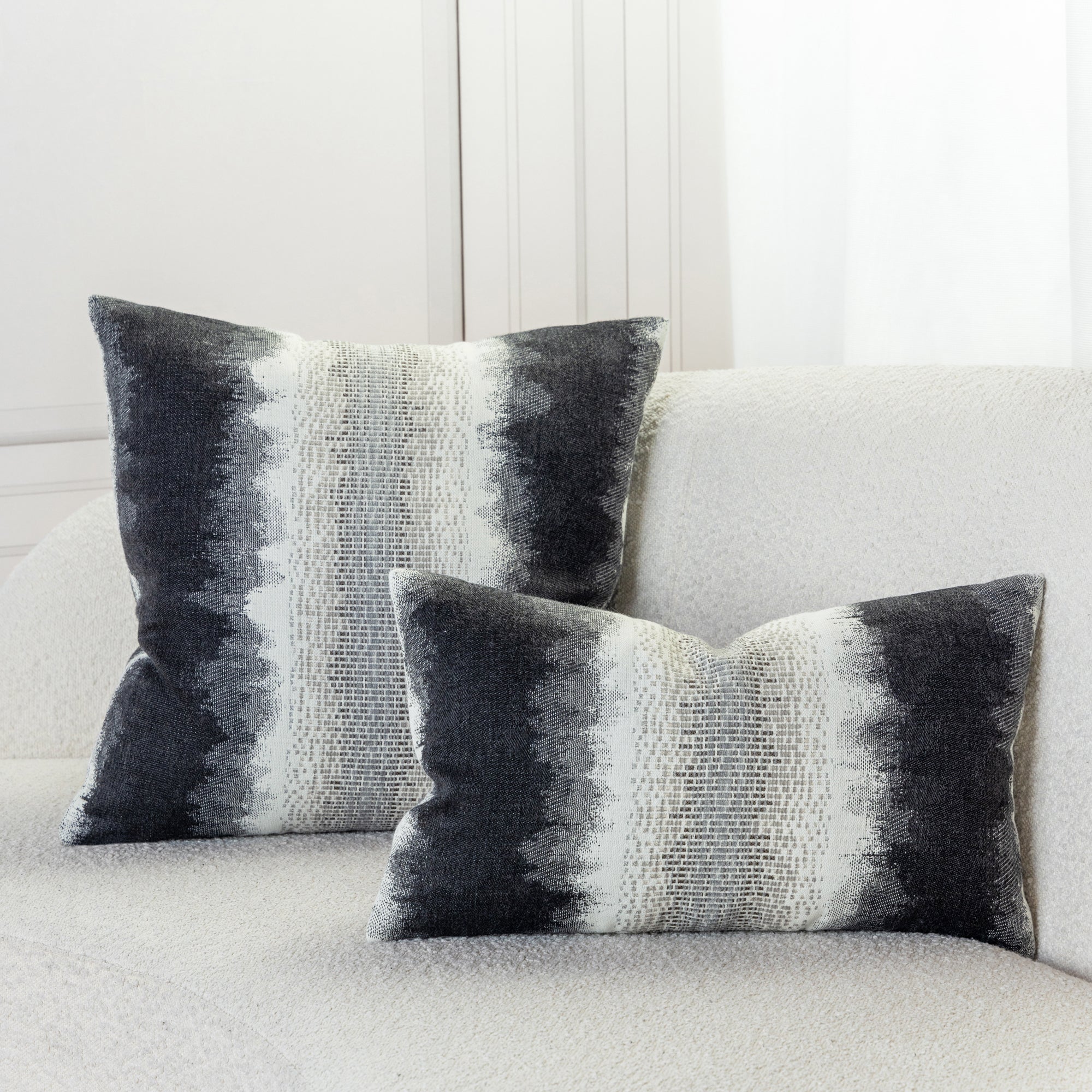 Indoor environmental image of pillows in charcoal and white with blended chenille block center band  in  outdoor safe woven fabric with ombre edge