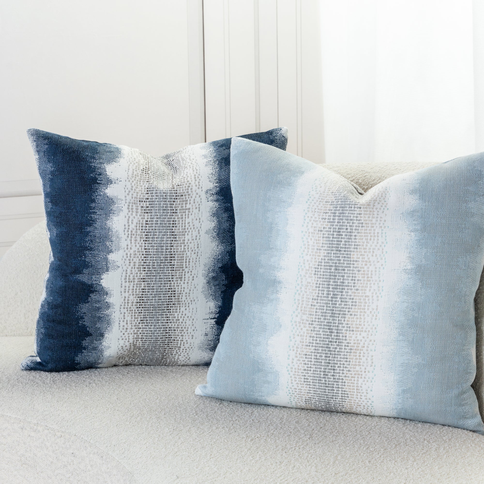 Indoor environmental image of pillows in Sky blue and white with blended chenille block center band  in  outdoor safe woven fabric with ombre edge