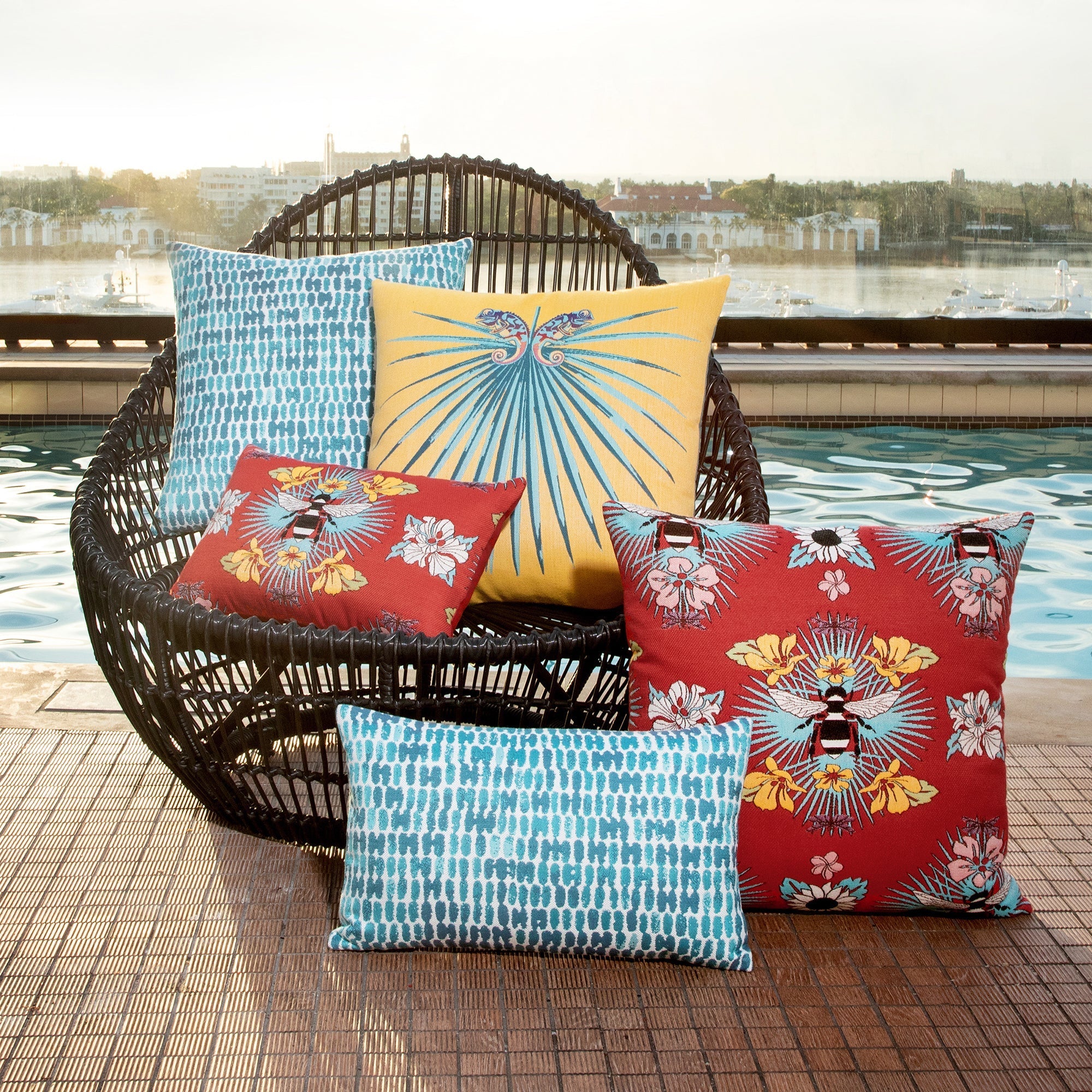 Outdoor image of pillows in Red outdoor safe fabric with tropical bee and floral motif featuring textured yarns and chenille accents