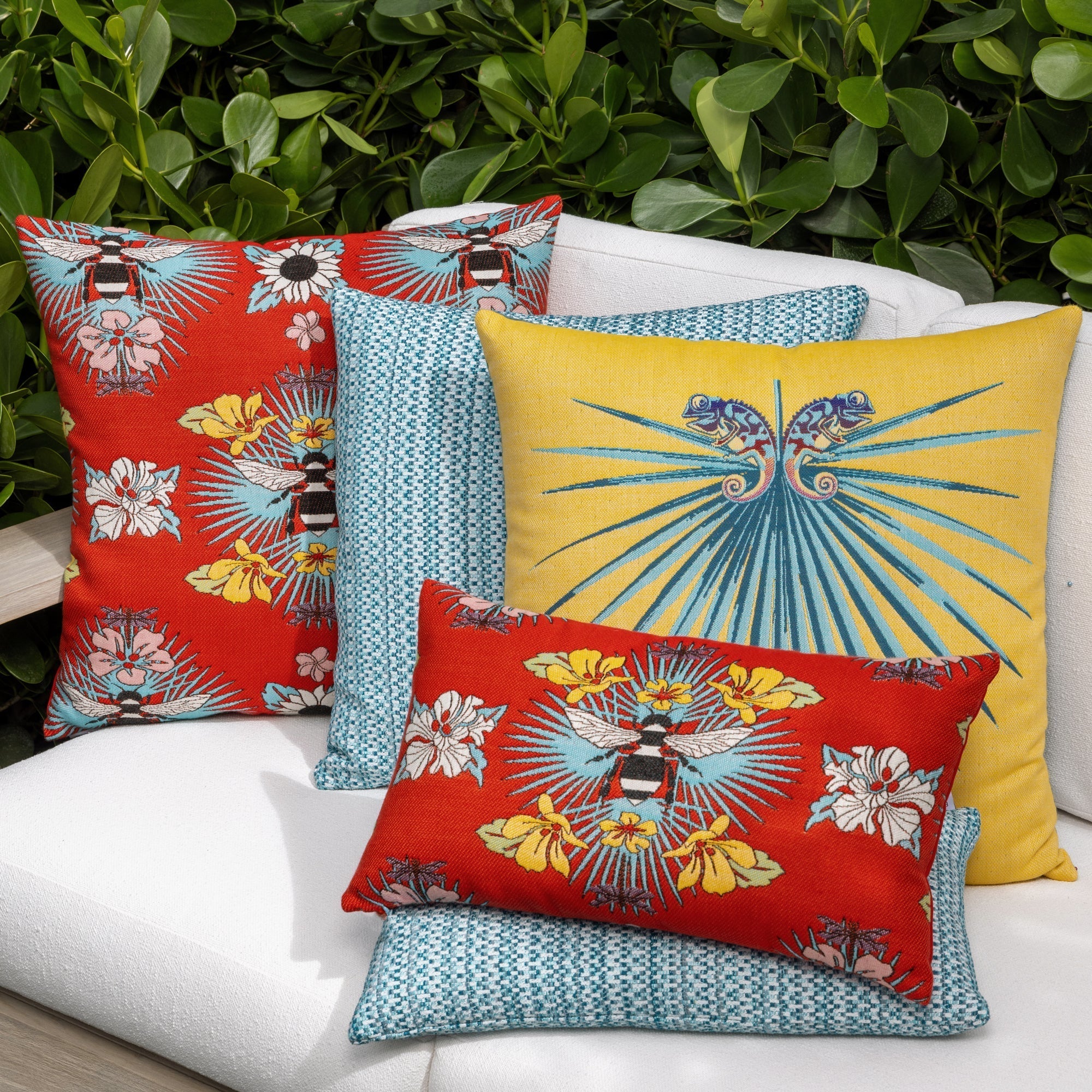 Outdoor image of pillows in Red outdoor safe fabric with tropical bee and floral motif featuring textured yarns and chenille accents