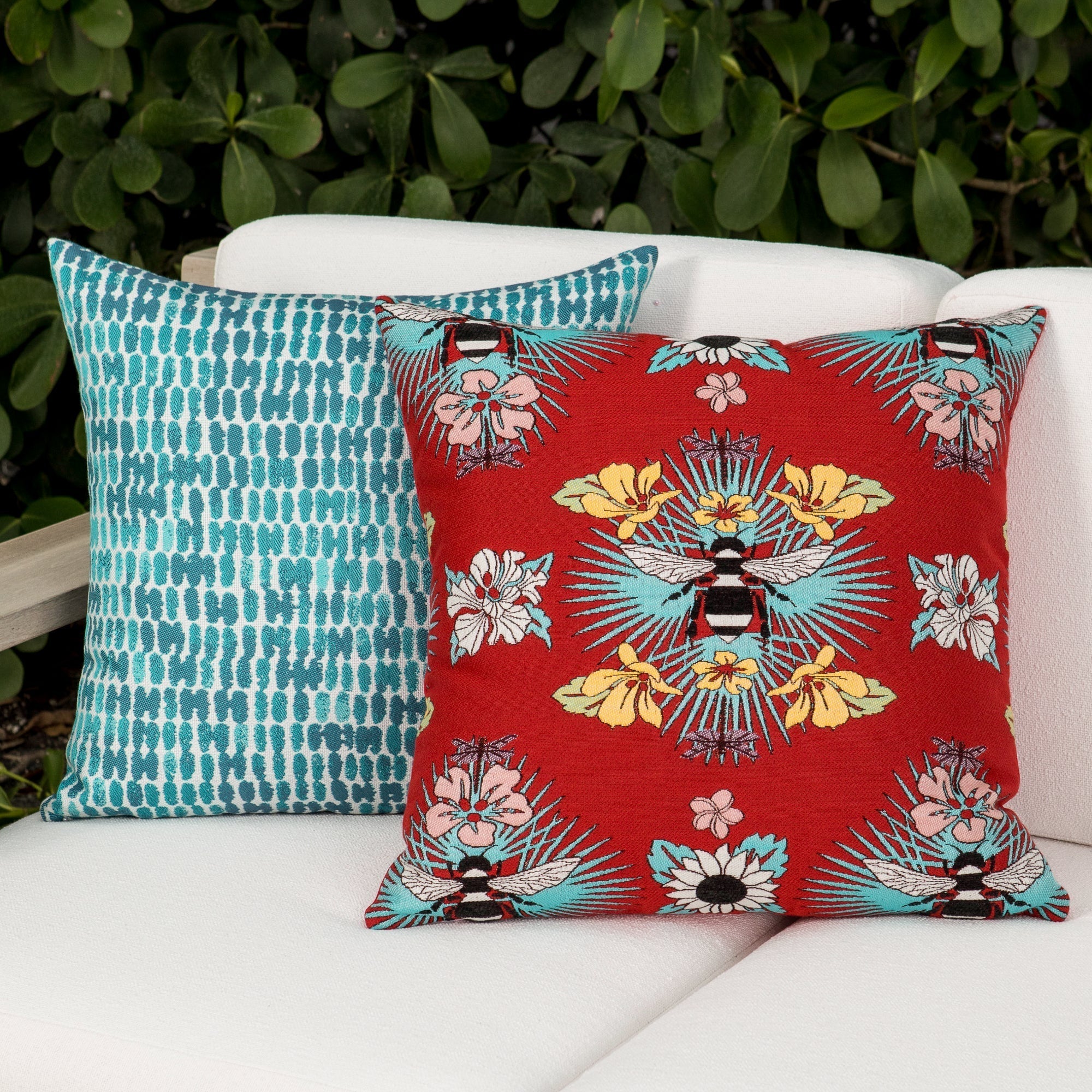 Outdoor image of pillows in Red outdoor safe fabric with tropical bee and floral motif featuring textured yarns and chenille accents
