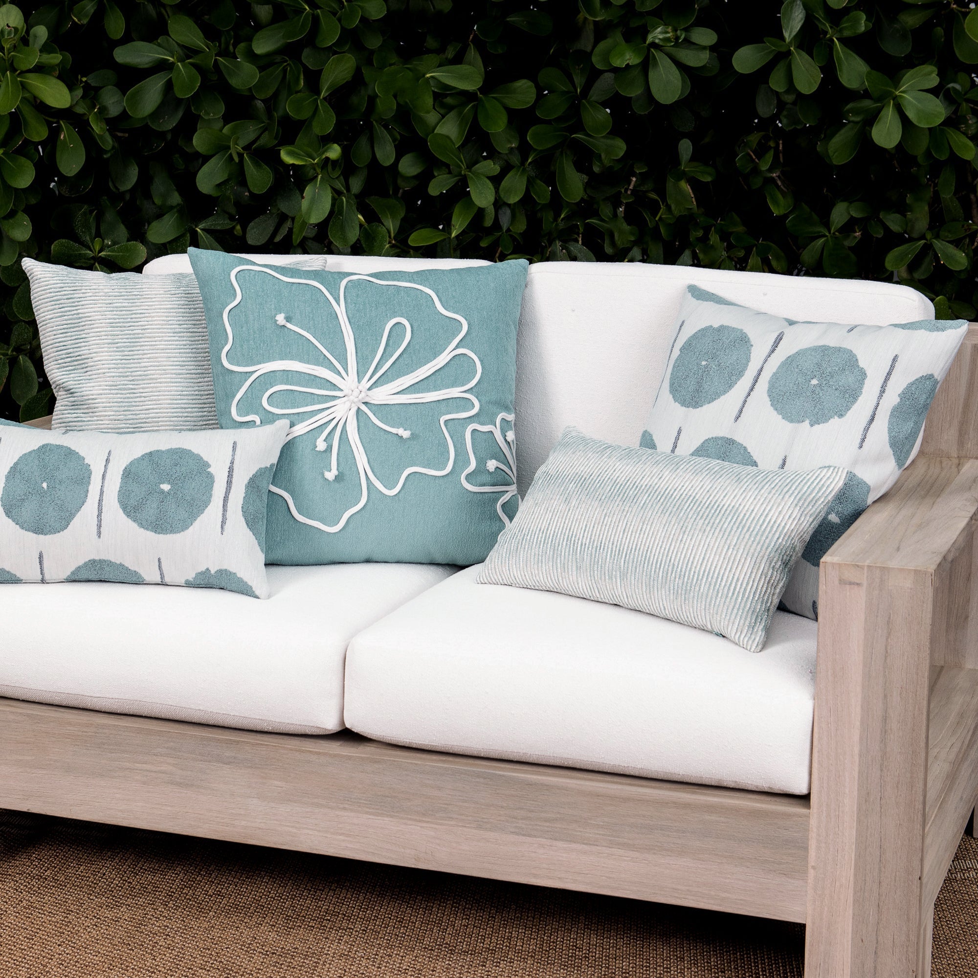 Luxury light blue subtle patterned decorative pillow on a woven outdoor sofa, featuring soft touch performance weave for residential and commercial interiors