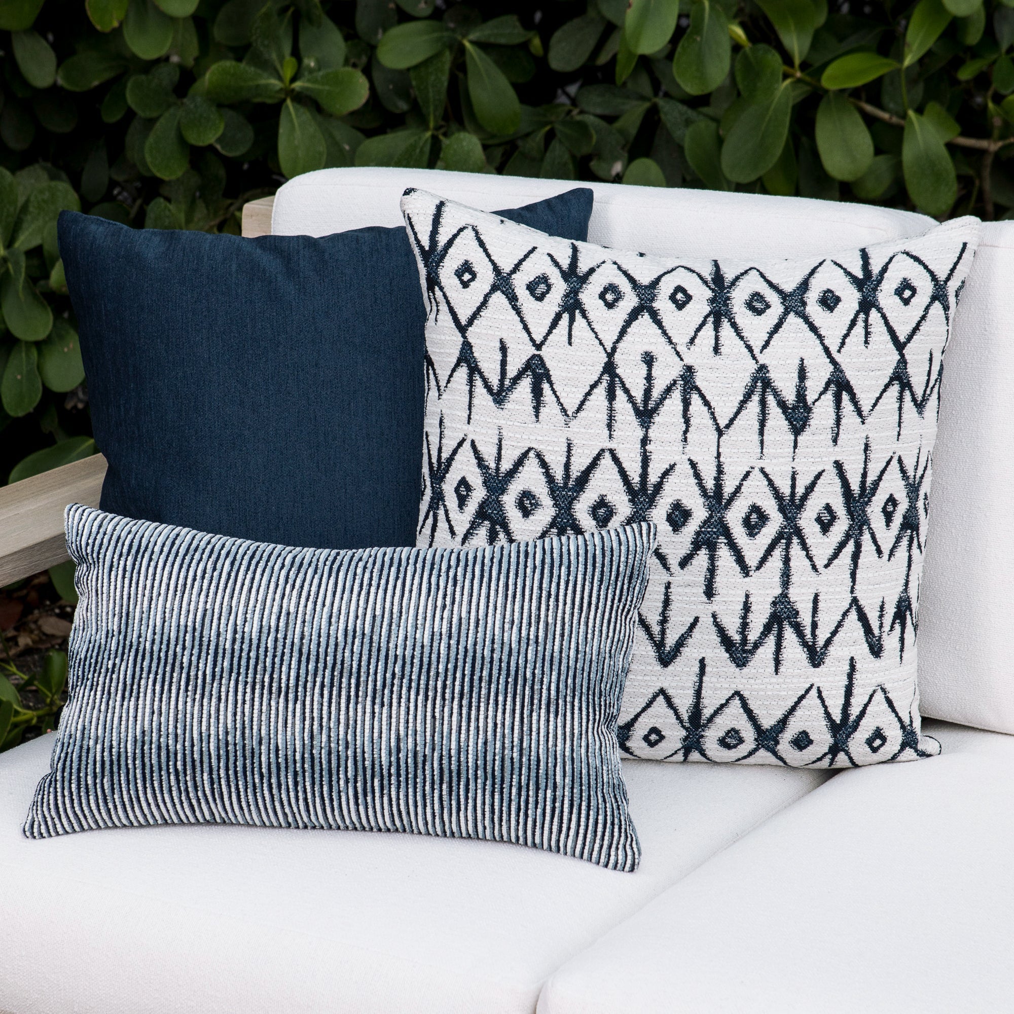 Outdoor image of pillows in Decorative pillows on a white outdoor sofa with green foliage in the background