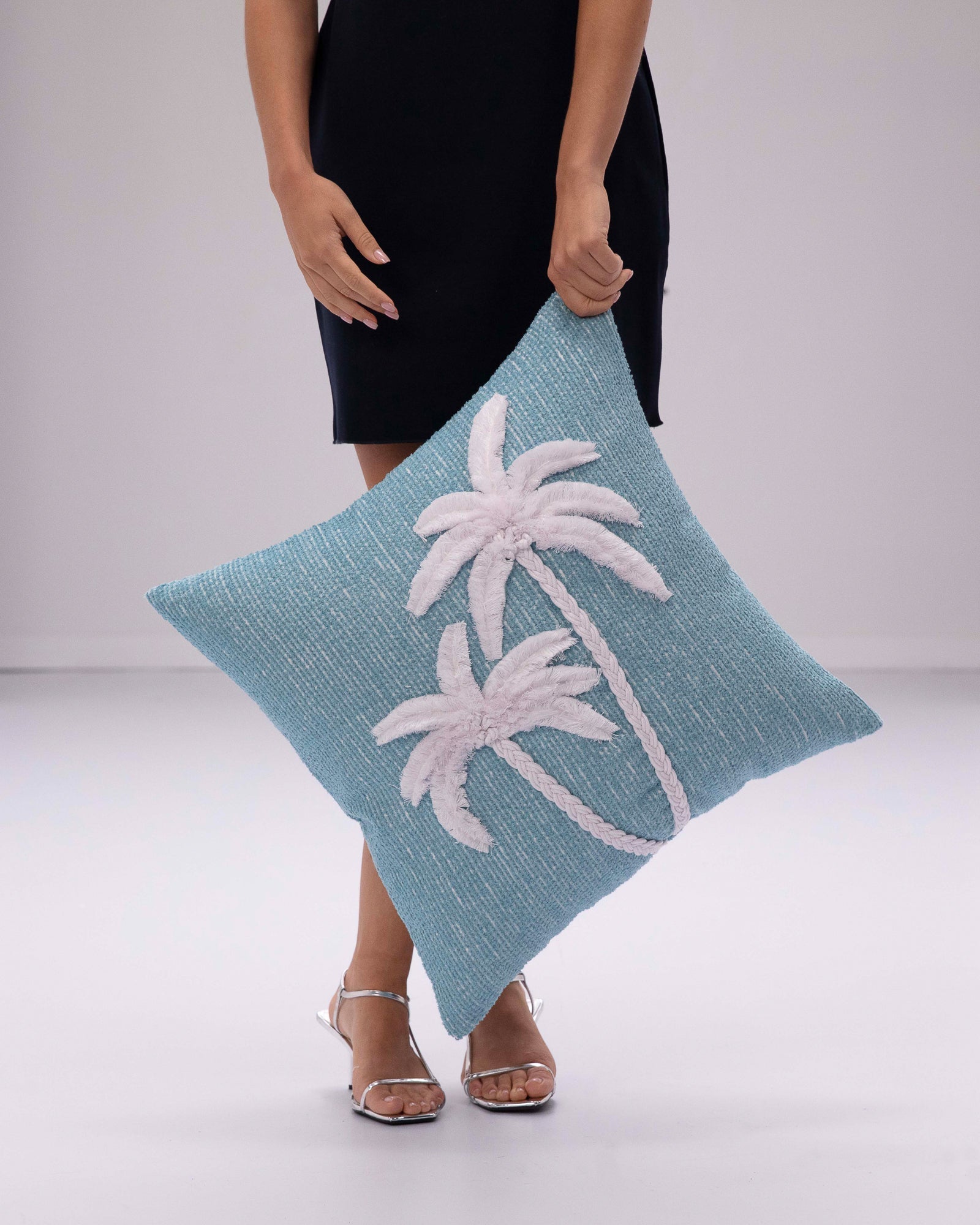 Person holding a blue pillow with white palm tree design on a plain background