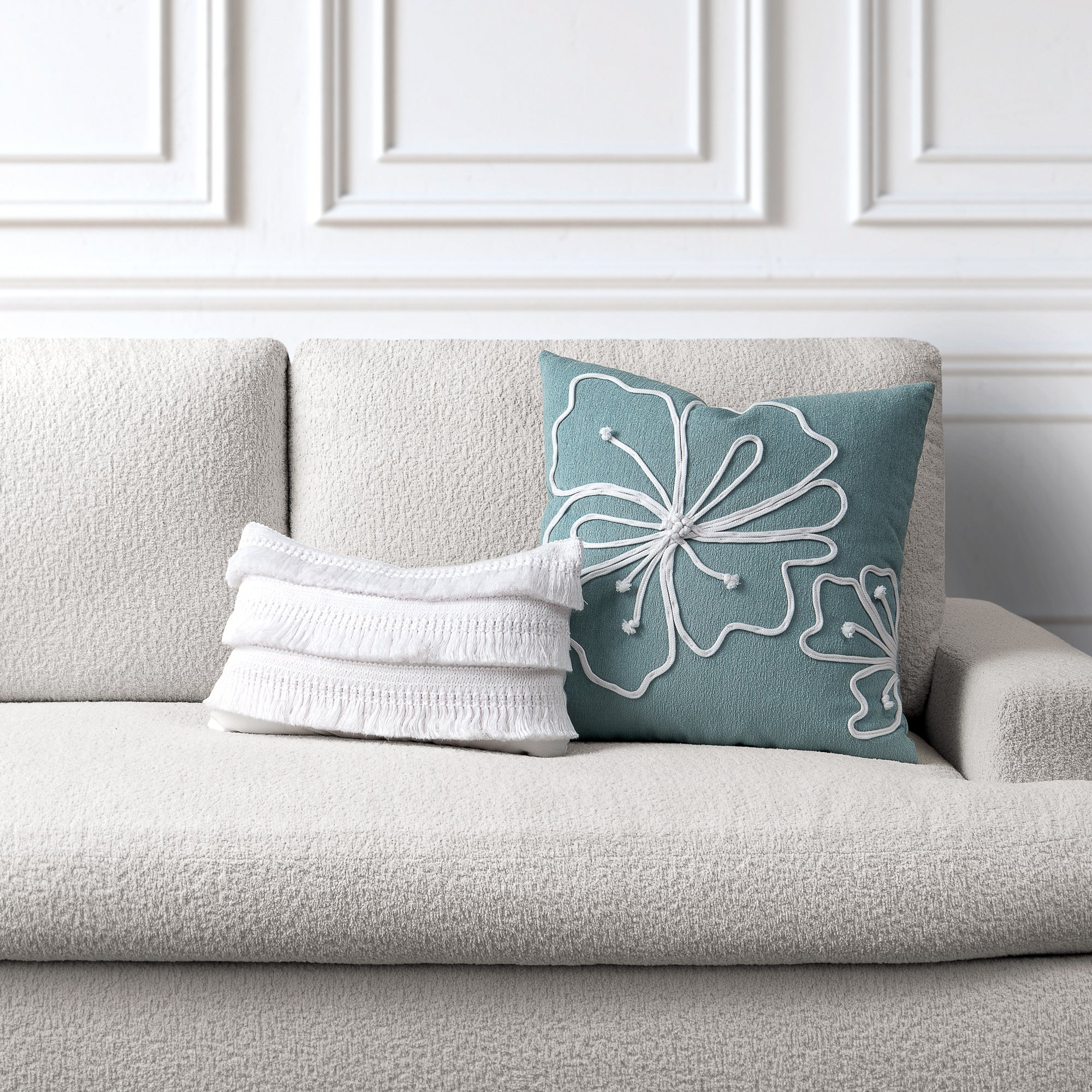 Gray sofa with a white textured throw pillow and a blue pillow with floral patterns against a white paneled wall.