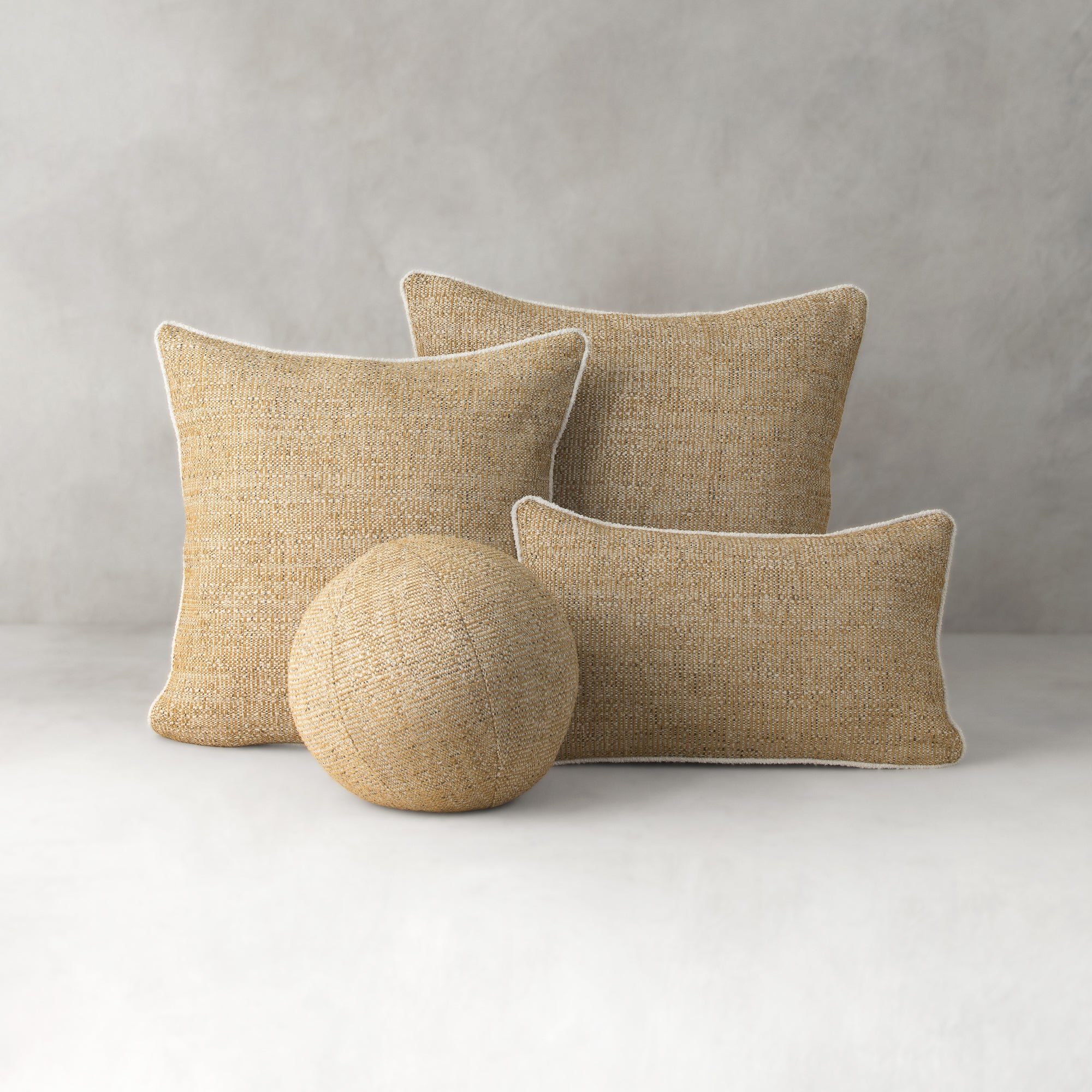 Three beige textured pillows and a spherical object on a light gray background
