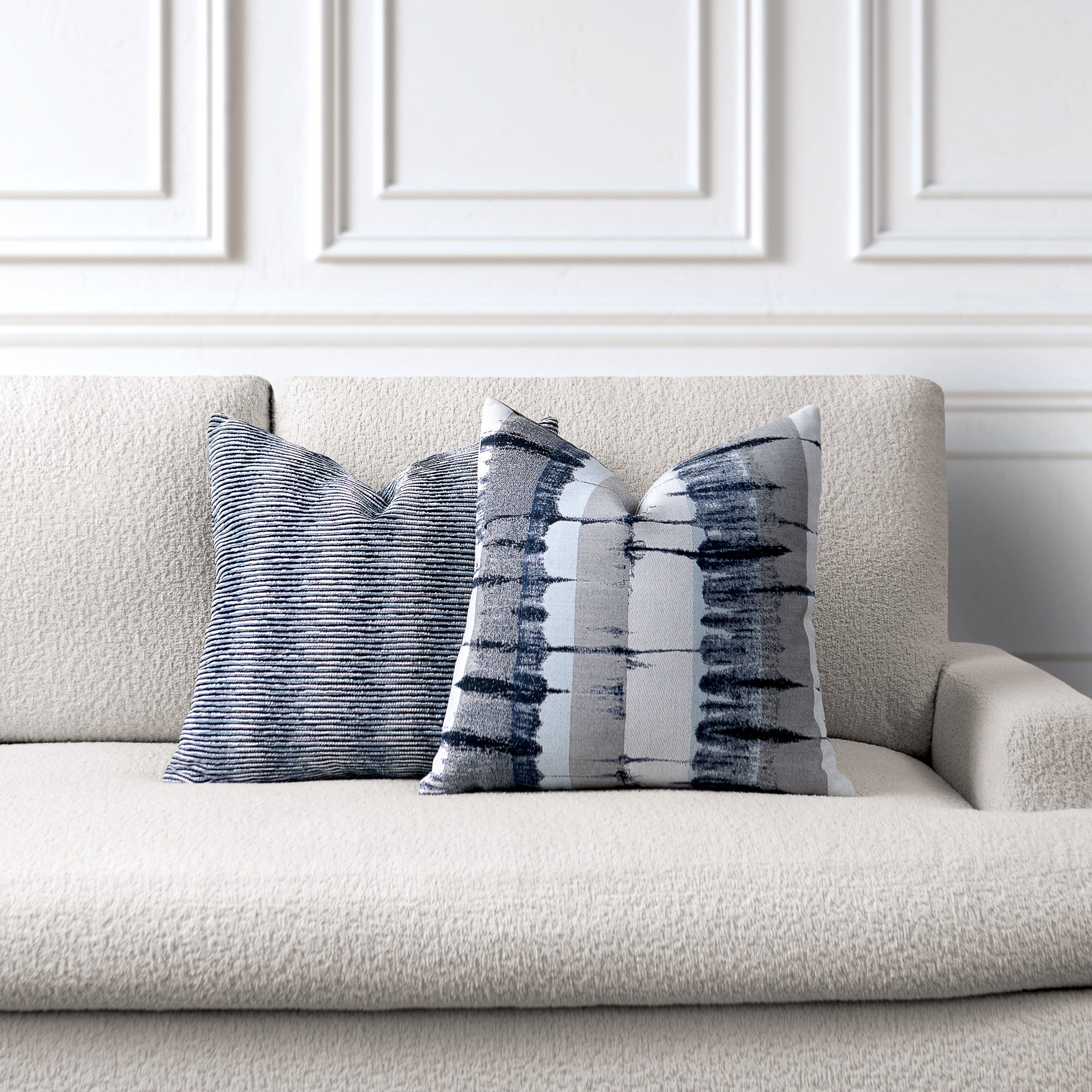 Decorative pillows with abstract patterns on a beige sofa against a white paneled wall.
