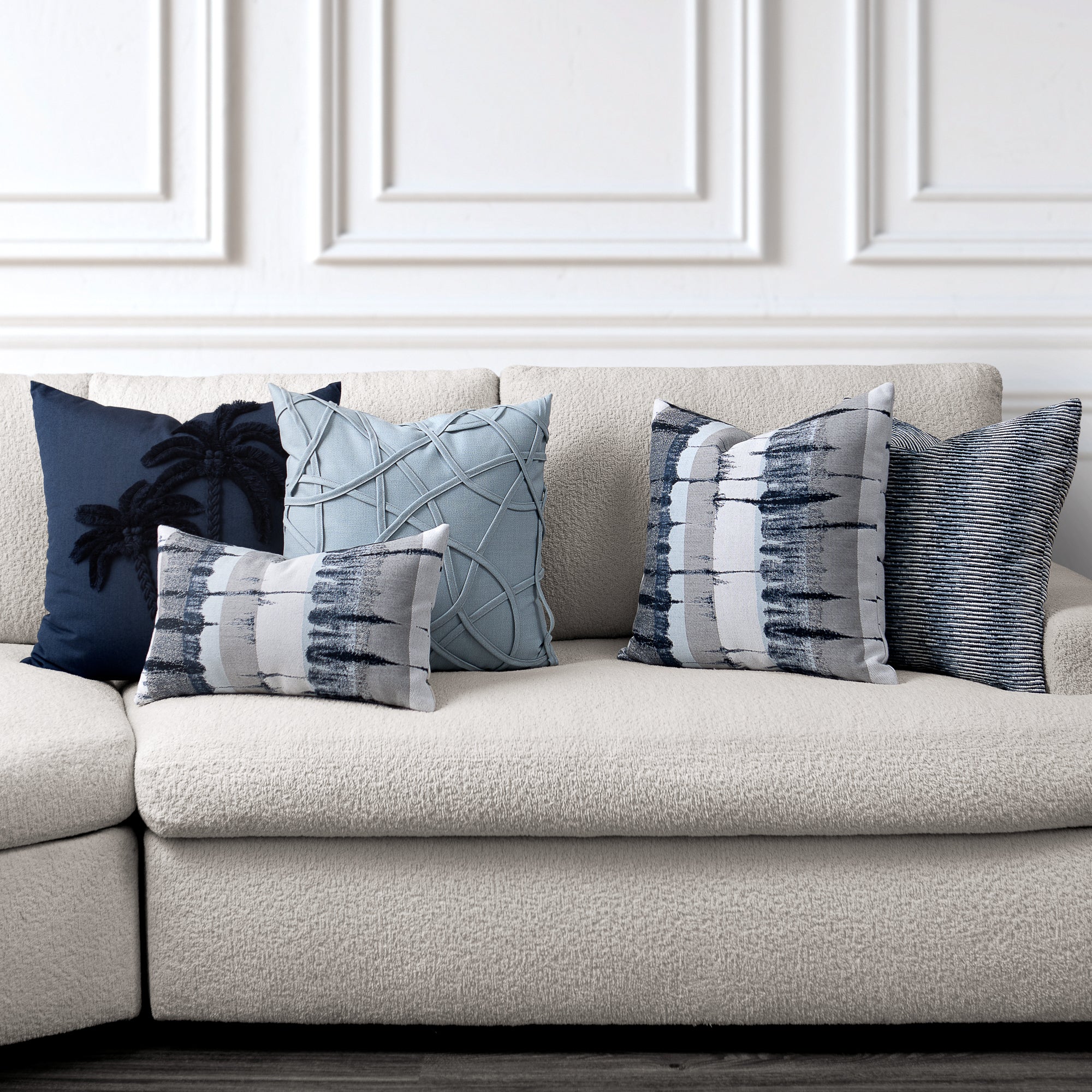 Beige sofa with decorative outdoor safe pillow package against a white wall