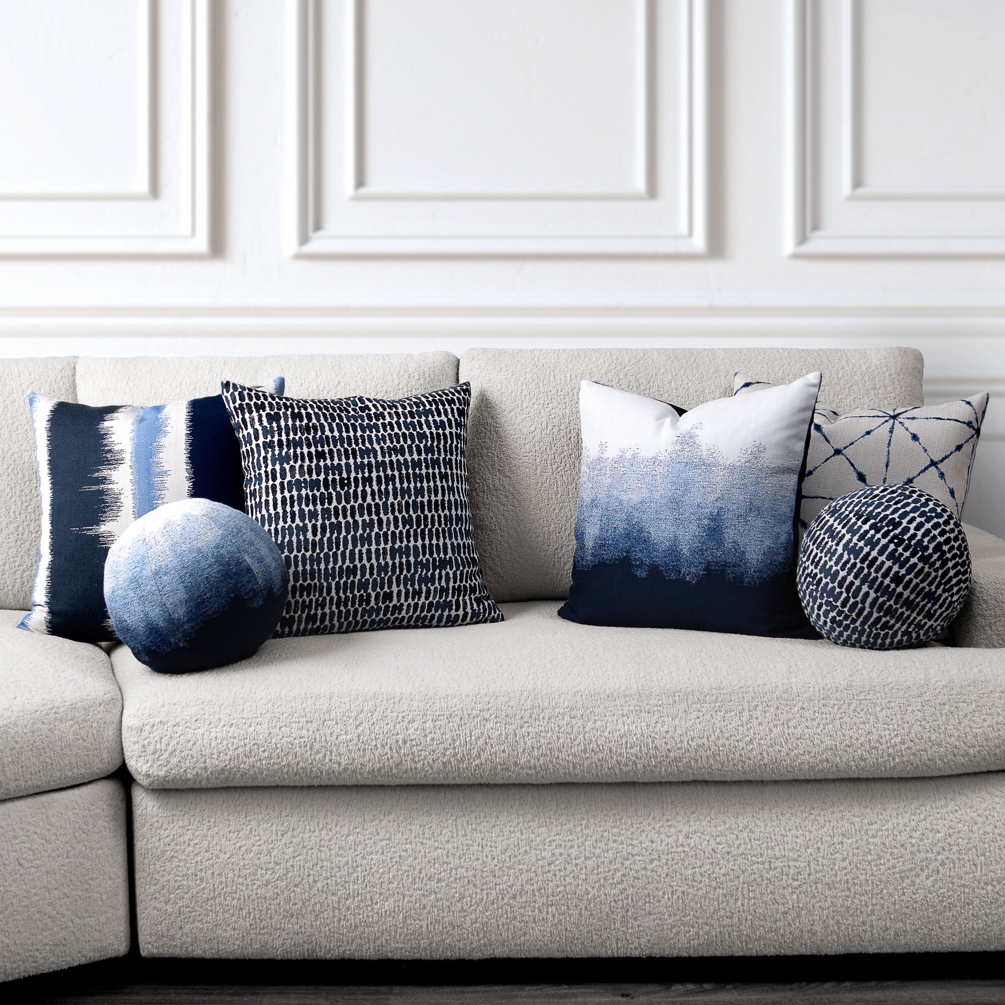 Gray sofa with decorative pillows featuring blue and white patterns in a room with white paneled walls. - outdoor safe by Elaine Smith