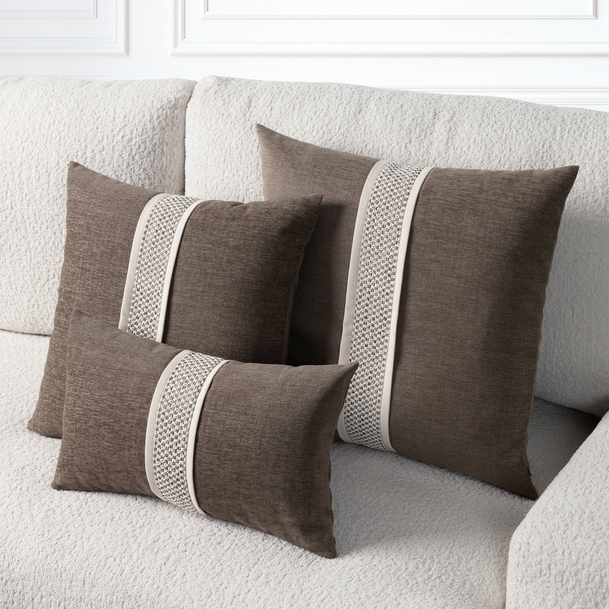 Three brown throw pillows with cream textured vertical stripes, arranged on a textured beige sofa.