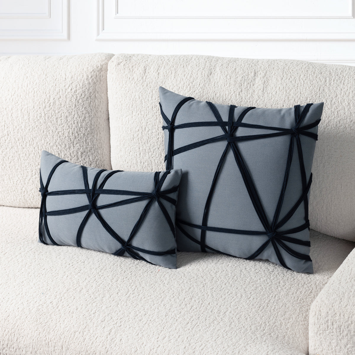 Two gray decorative throw pillows with black geometric ribbon-like trim, displayed on a textured cream boucle sofa.