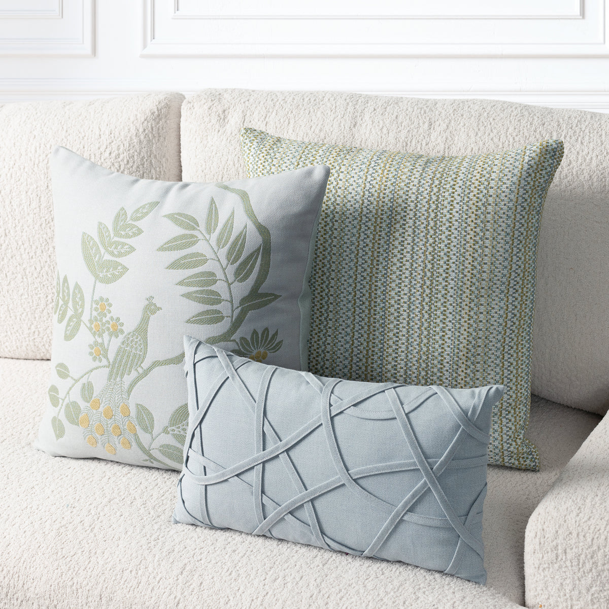 Three decorative throw pillows arranged on a cream boucle sofa. The front pillow is light blue with a raised crisscross lattice pattern.