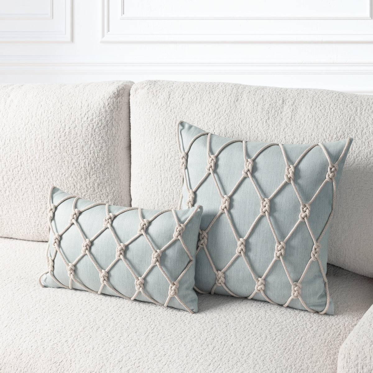 Two square decorative throw pillows in a pale blue-gray fabric with a beige rope knotted lattice pattern, styled on a textured cream boucle sofa.