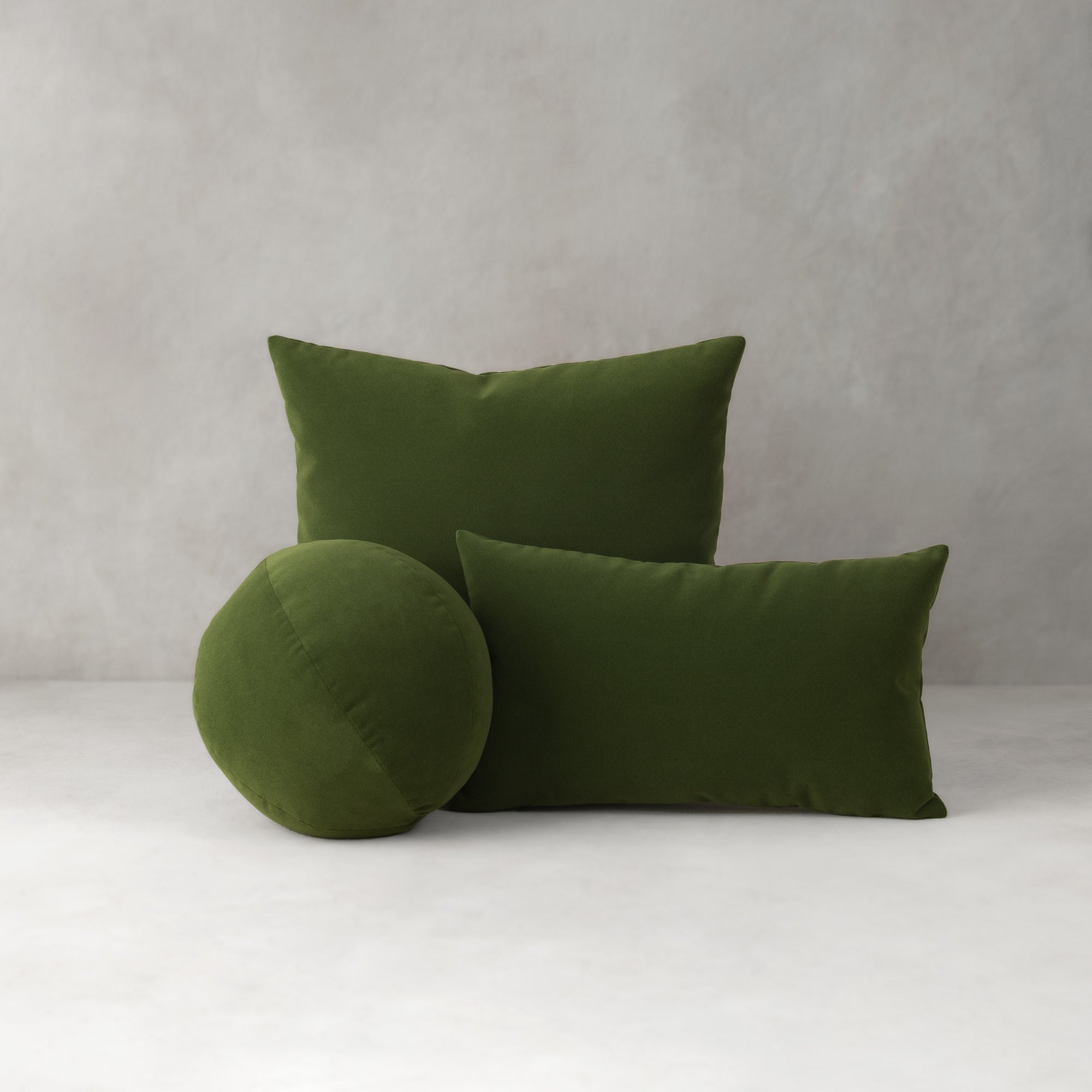 Three green pillows on a white surface with a gray background