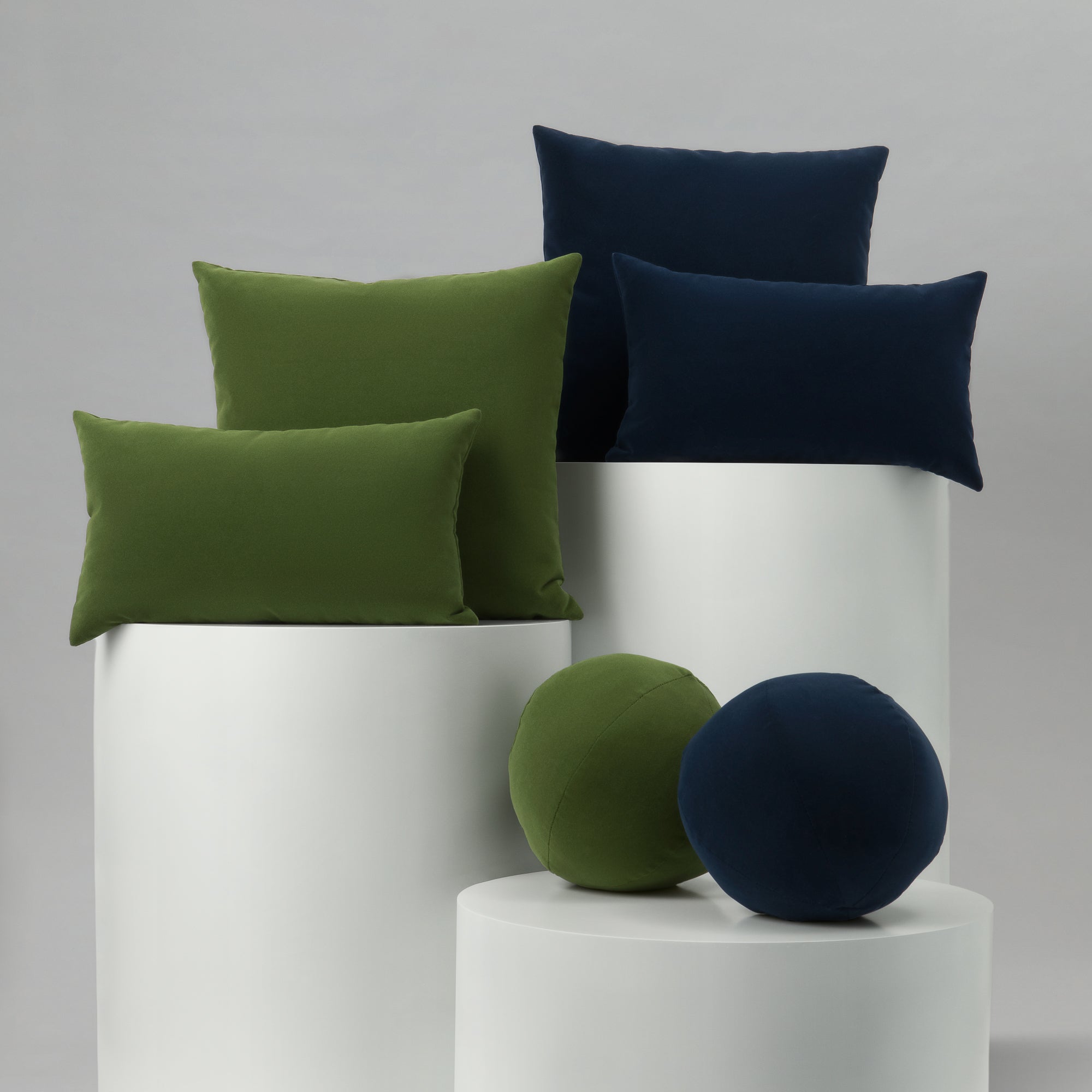 Green and navy cushions on white cylindrical stands against a gray background