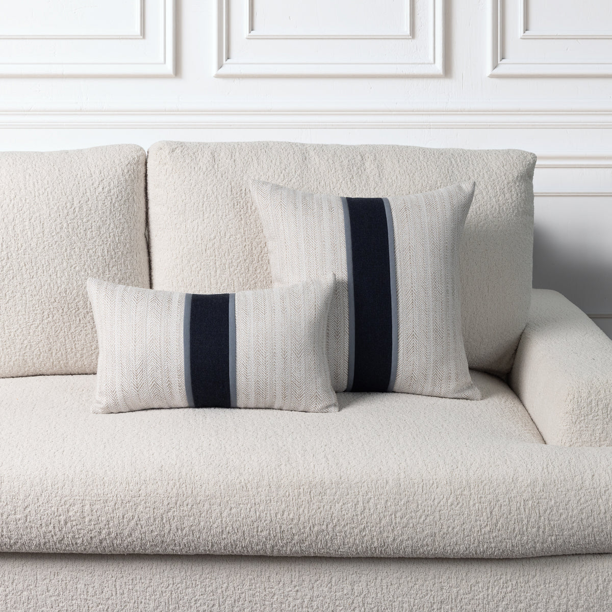 Two textured throw pillows with vertical navy and gray stripes, styled on a cream bouclé sofa against a white paneled wall.