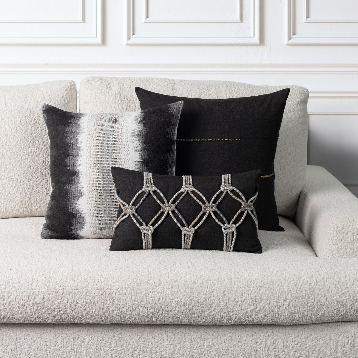 Three decorative throw pillows in black and white displayed on a textured cream boucle sofa against a white paneled wall.