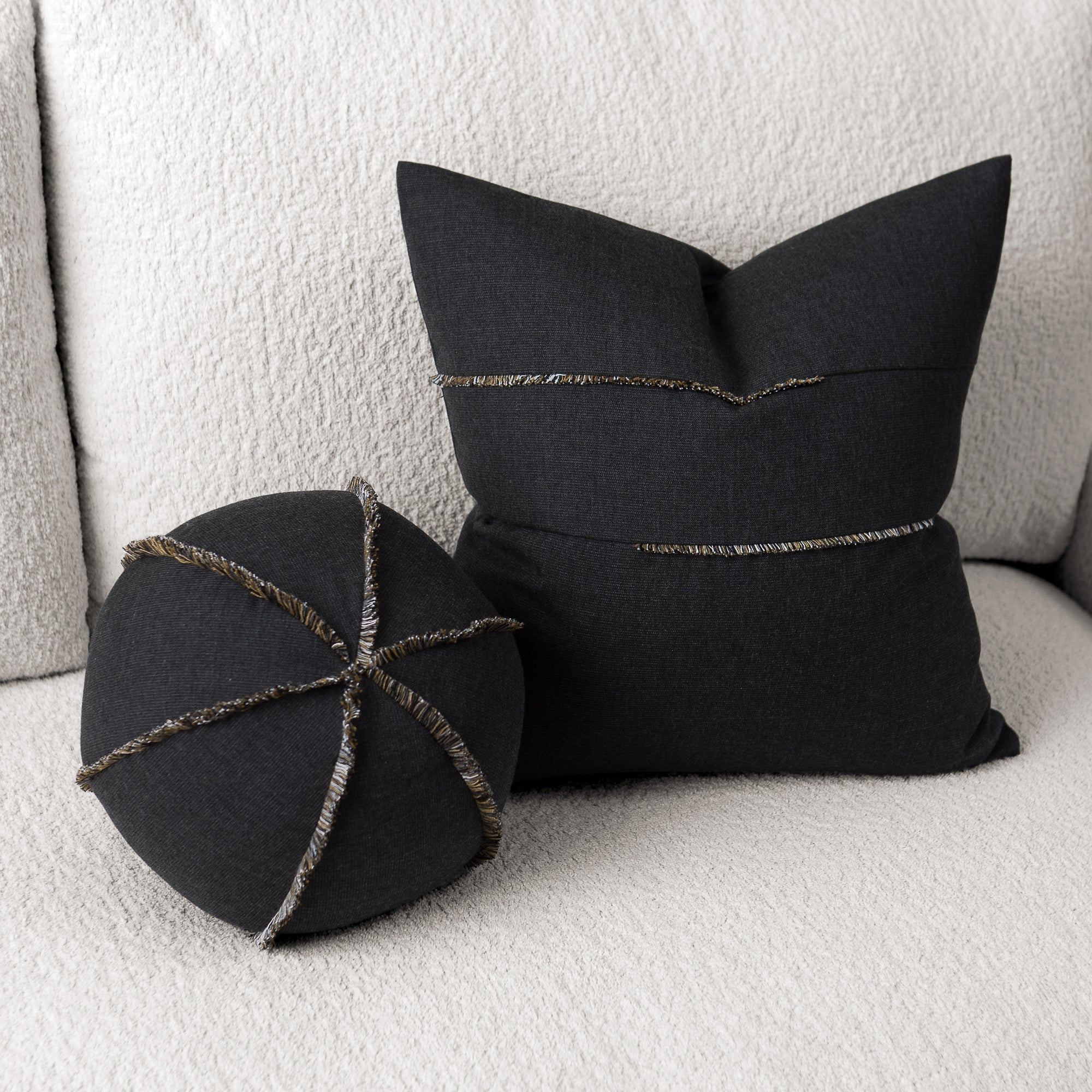 Two black pillows with decorative stitching on a light gray sofa.