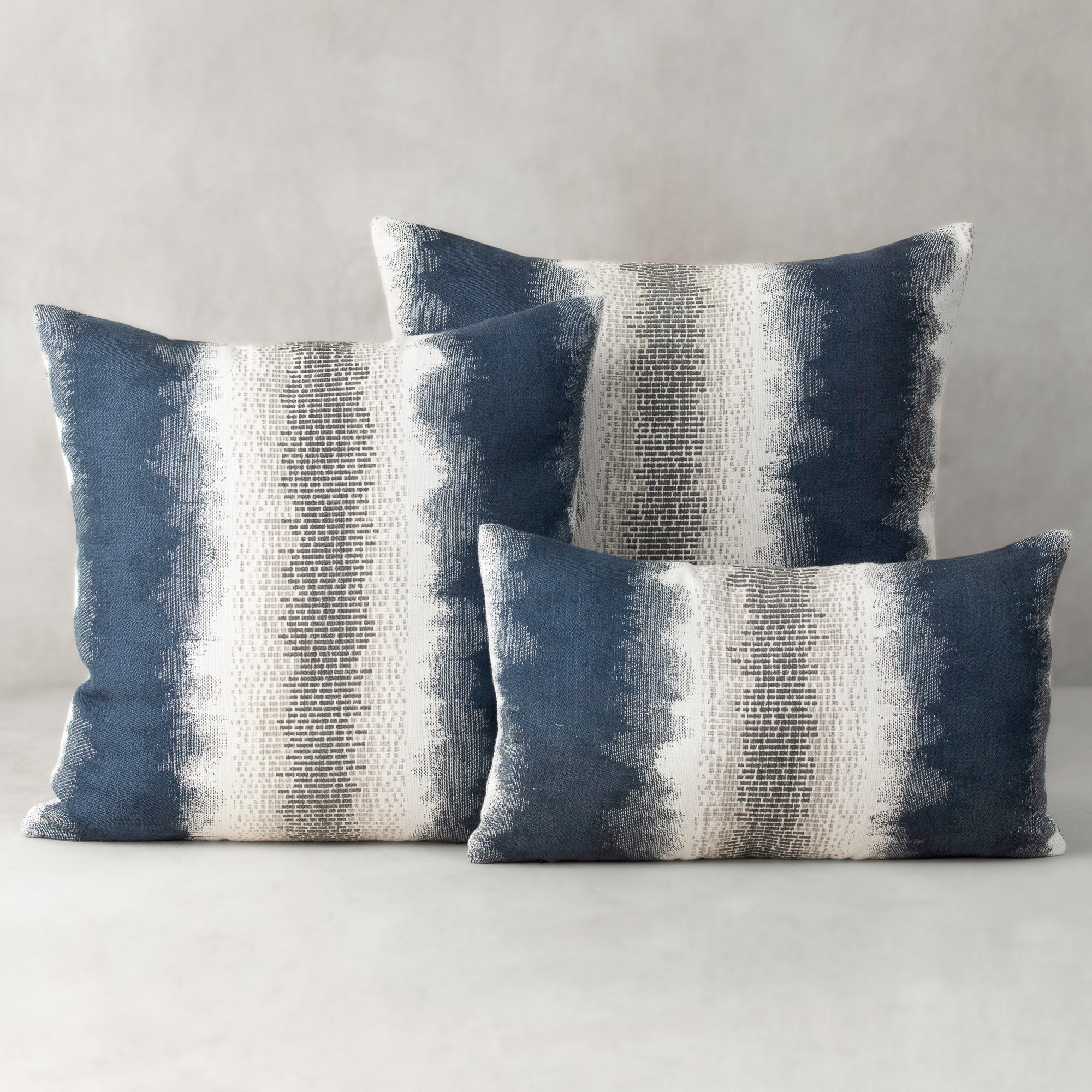 Three blue and gray striped pillows on a neutral background