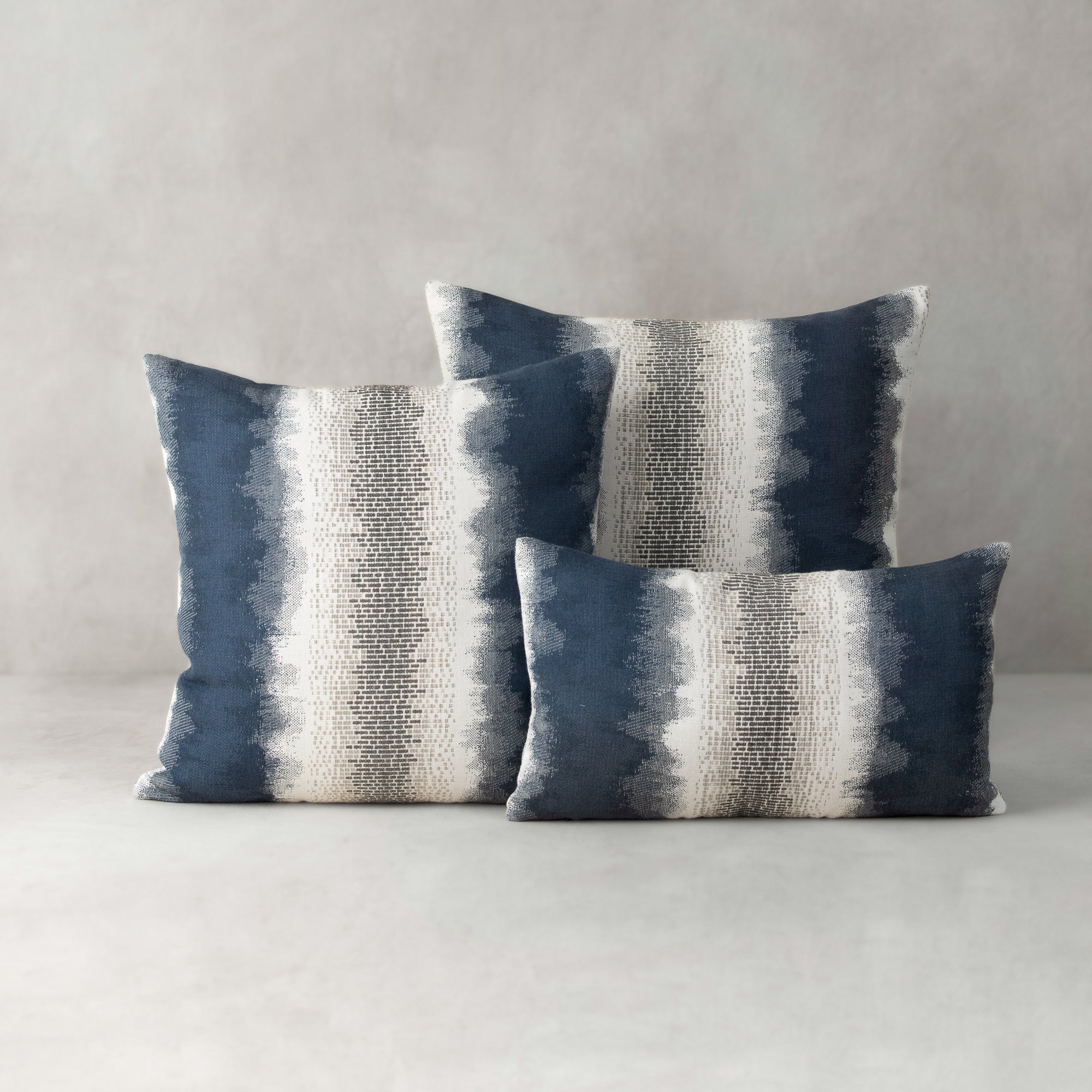 Three blue and gray striped pillows on a neutral background