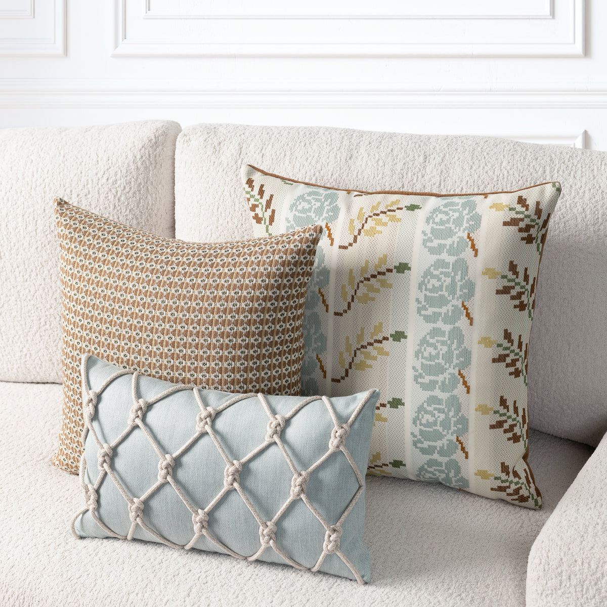 Three decorative throw pillows arranged on a textured cream sofa. The front pillow is light blue with a beige knotted lattice pattern.