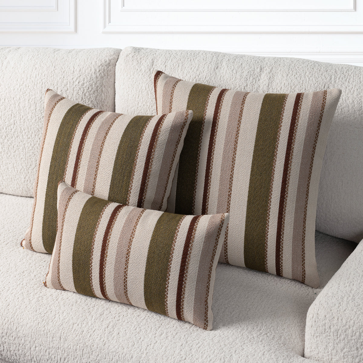 Three striped throw pillows in beige, brown, and olive green tones arranged on a textured cream sofa.