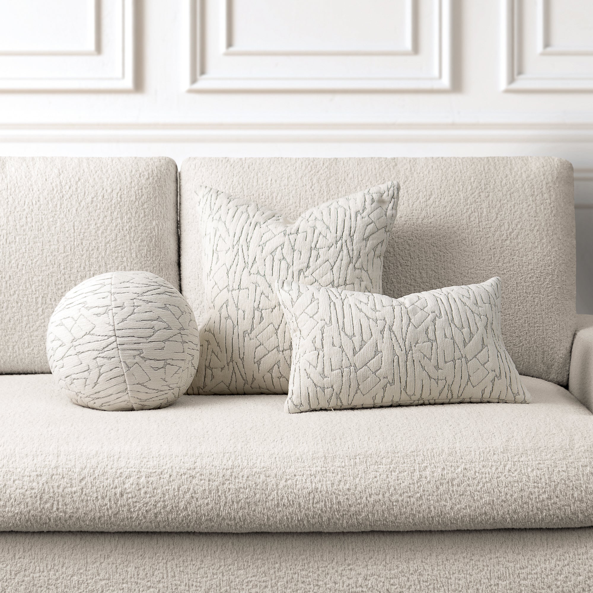 Textured pillows on a light gray sofa against a white paneled wall.