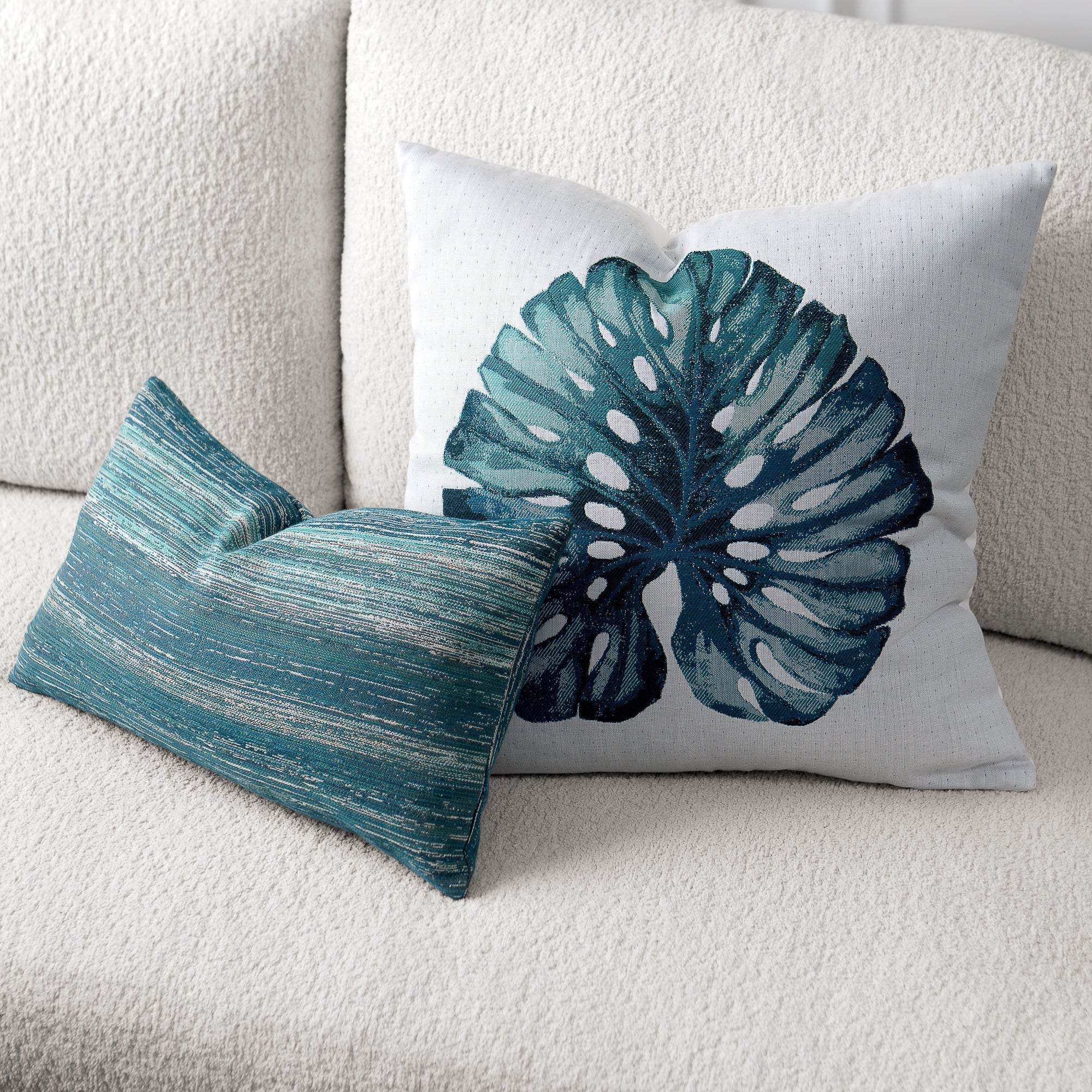 Two decorative pillows on a light-colored sofa, one with a leaf pattern and the other with a textured design.