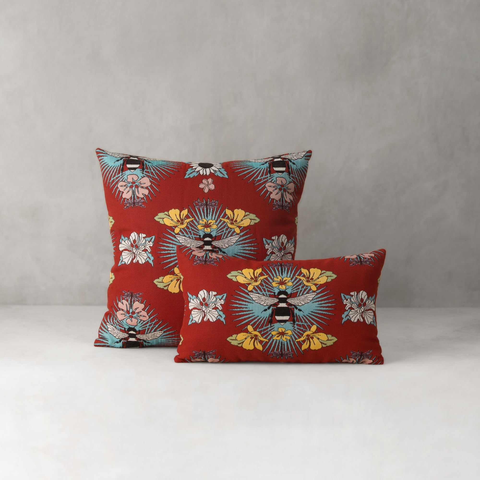 Two red pillows with floral and bee pattern on a gray background