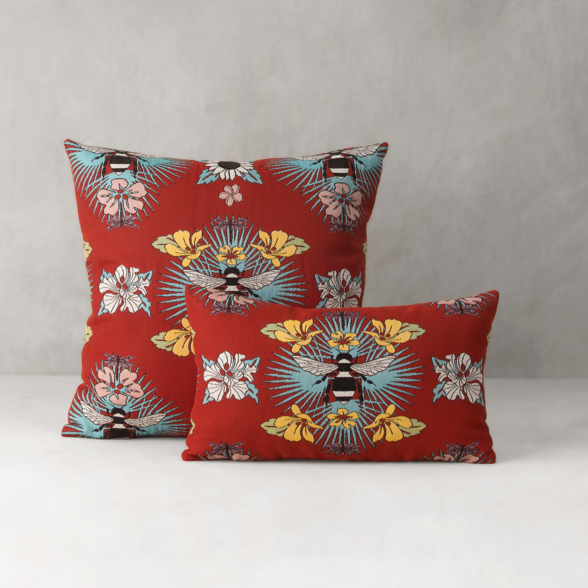 Two red pillows with floral and bee pattern on a gray background