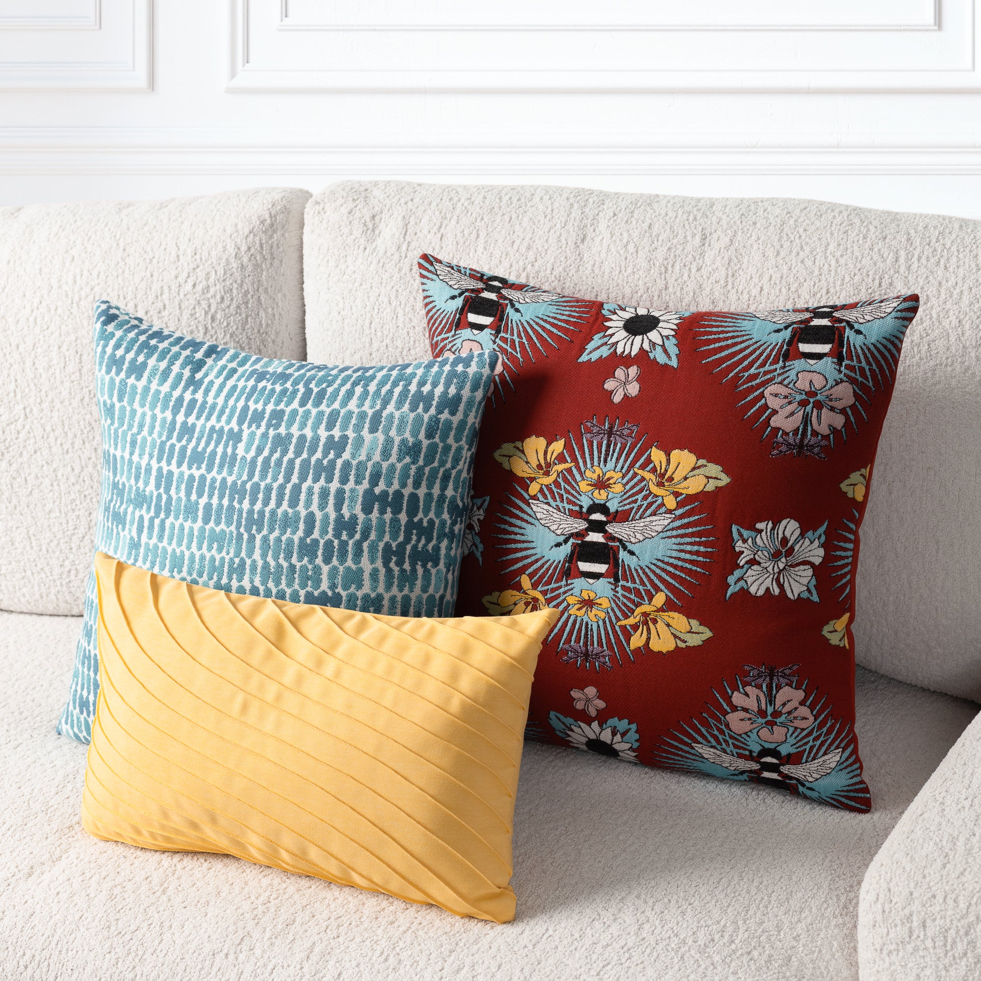 Three decorative throw pillows arranged on a light beige textured sofa. The front pillow is mustard yellow with a pleated texture.