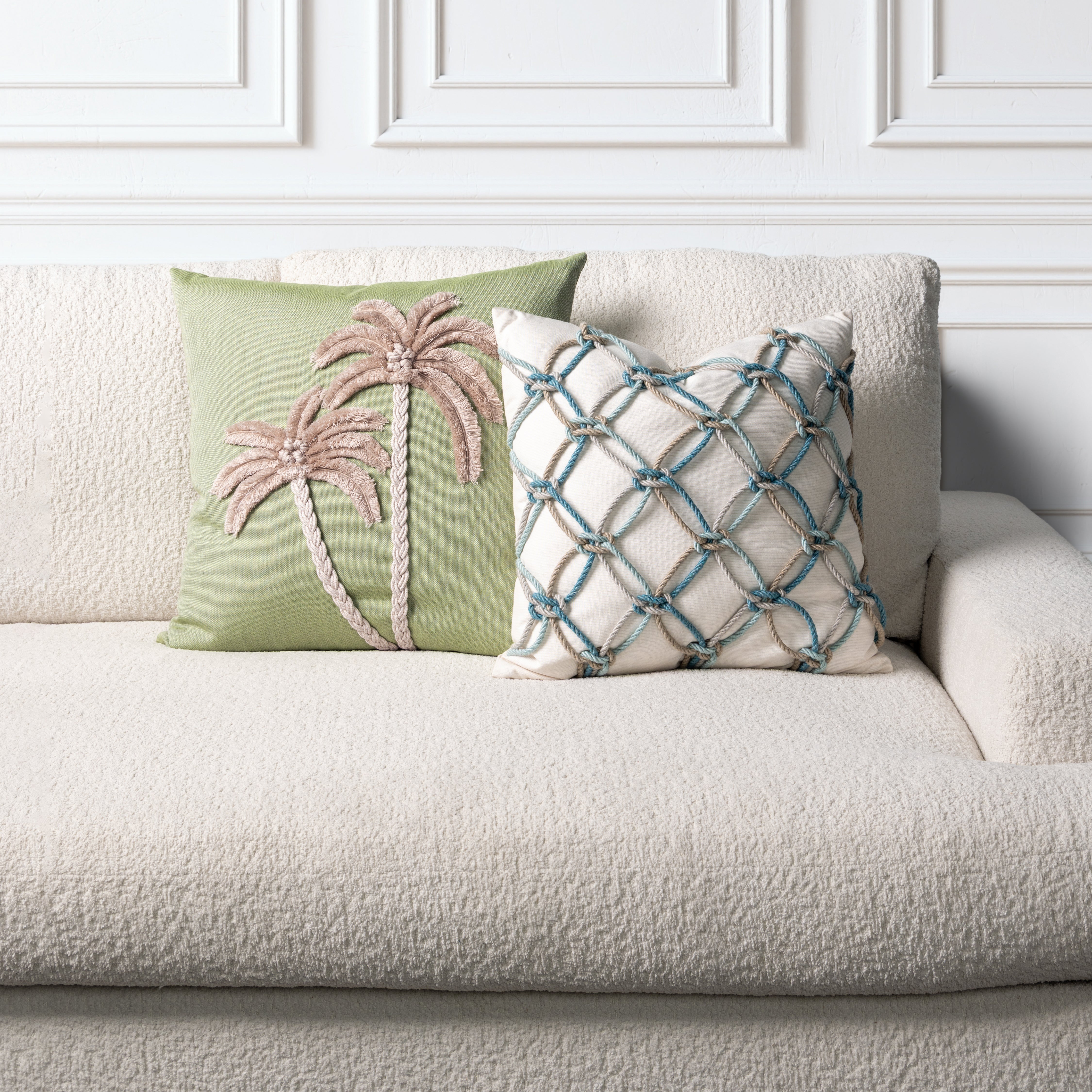 Two decorative pillows on a beige sofa with a white paneled wall background.